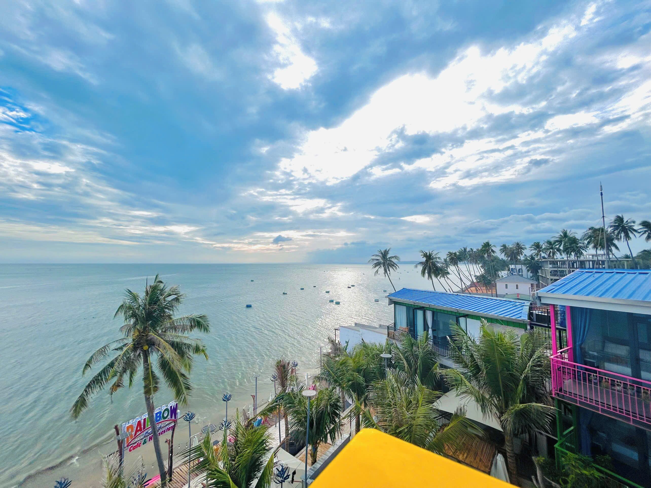 A coastal view with a beach, palm trees, and a building with a blue roof.
