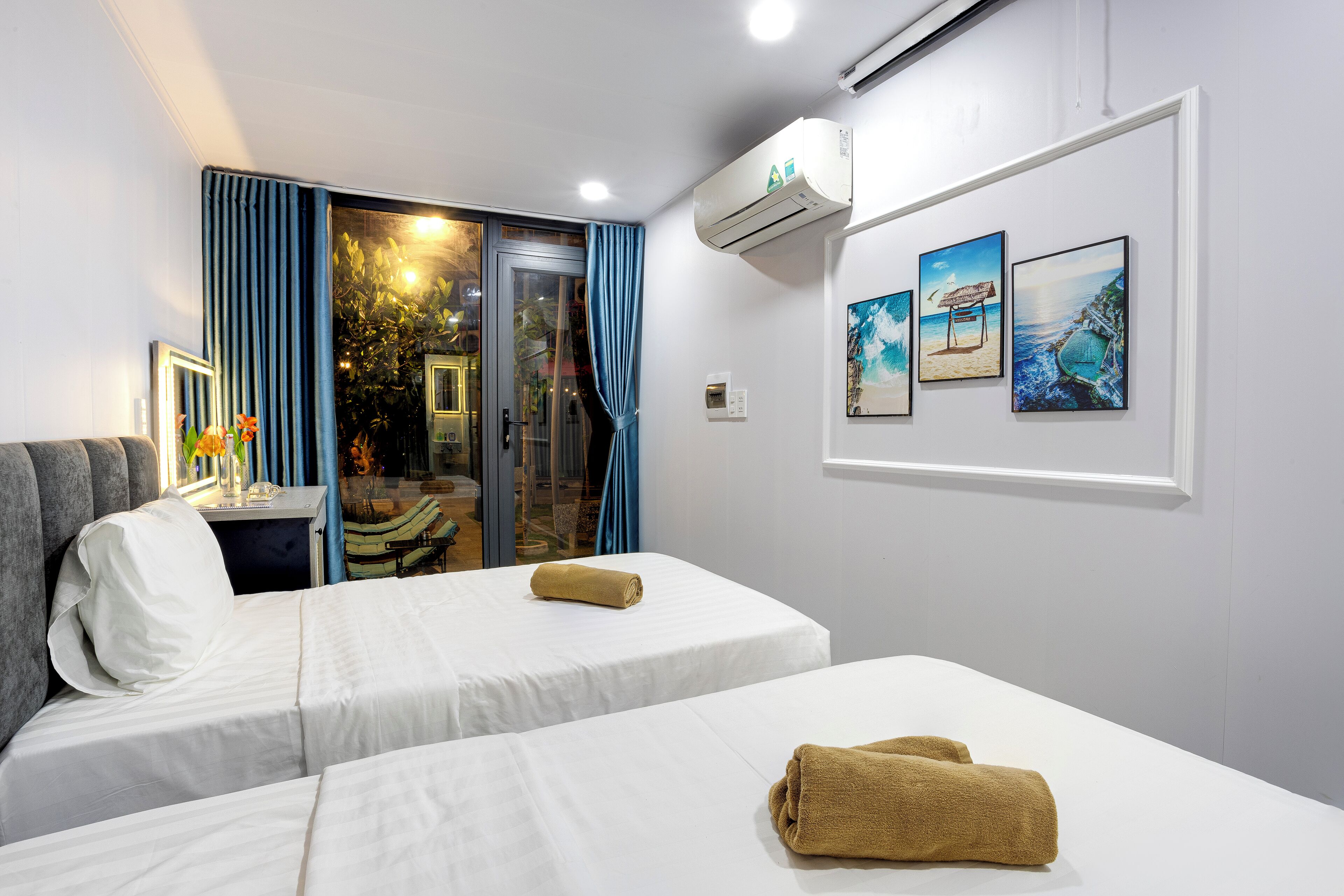 Quarto de hotel com duas camas, uma porta de vidro deslizante para uma varanda e três quadros na parede.