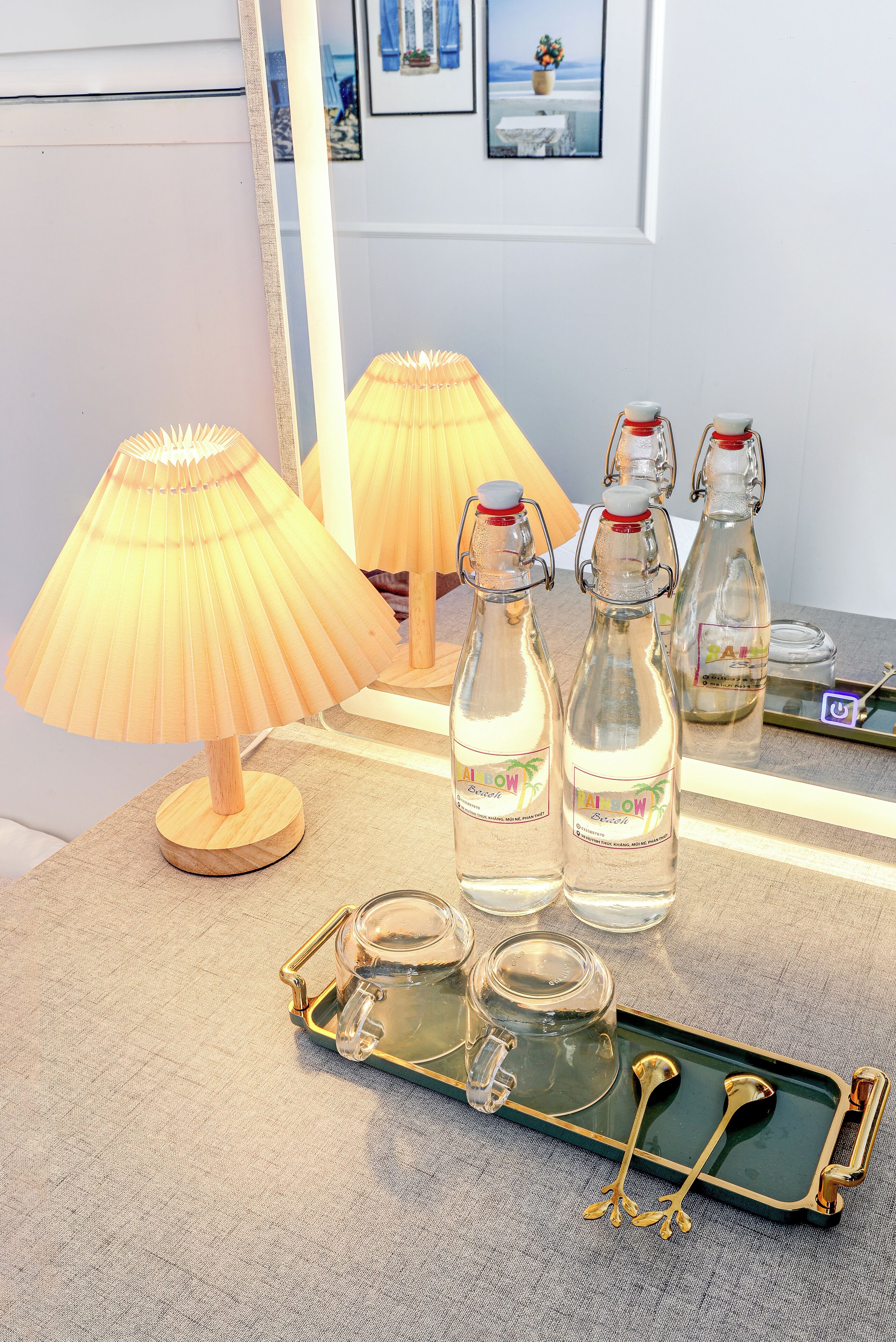 A table with a lamp, two bottles, and a tray with spoons.