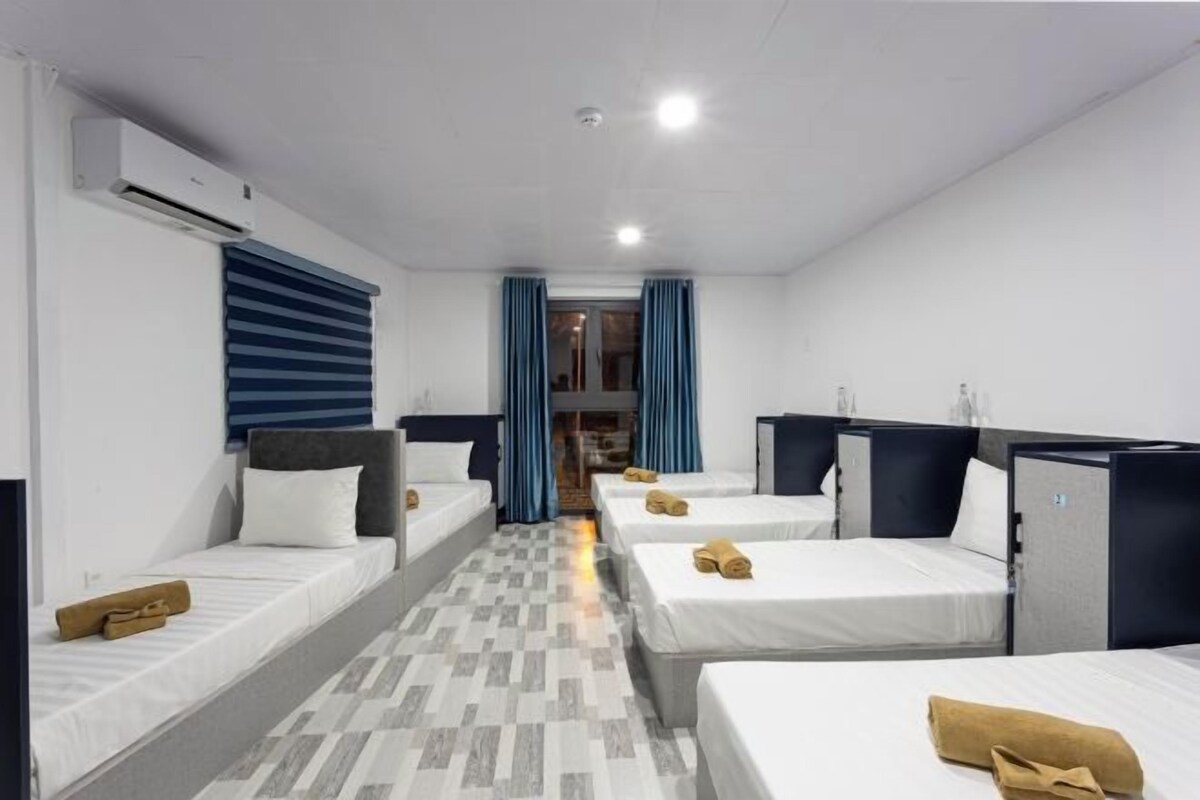 A hotel room with four single beds, a small kitchenette, a bathroom, and a view of the street.