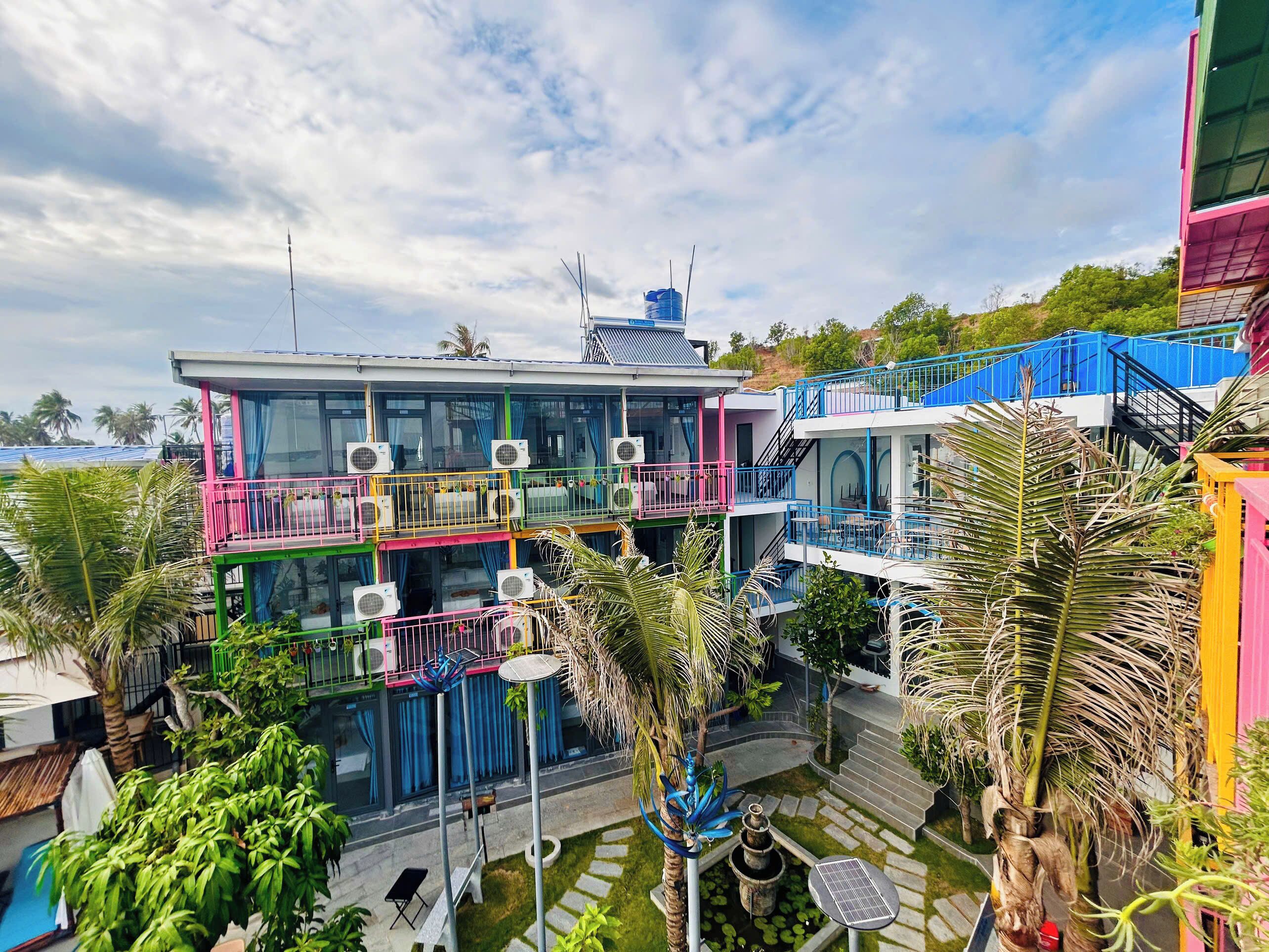 A multi-story building with balconies, air conditioning units, and a garden area with palm trees and a water feature.