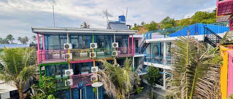A multi-story building with balconies, air conditioning units, and a garden area with palm trees and a water feature.