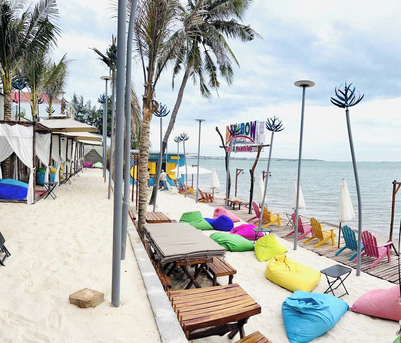 A beachside resort with colorful bean bags, wooden tables, and beach chairs.