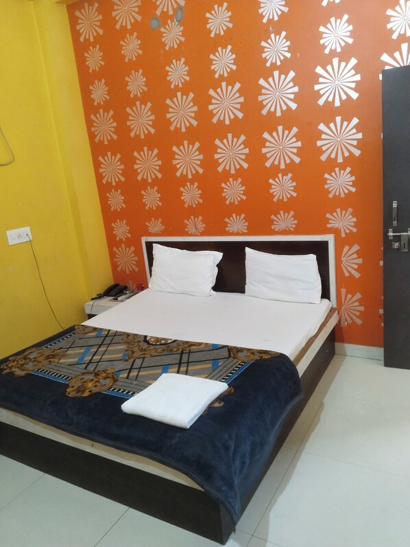 A bed with white pillows and a blue blanket, a telephone, and a wall with a geometric pattern. - HOTEL PINK CITY (Sikar)