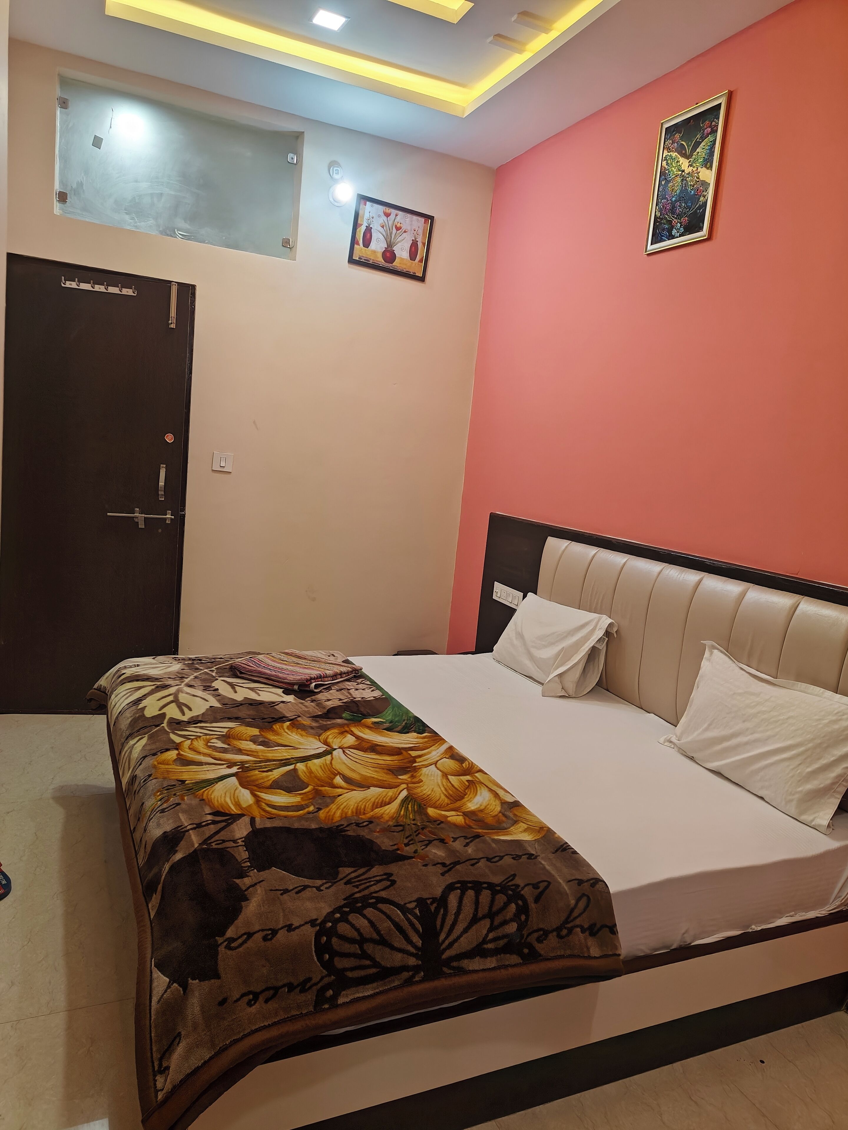 Un dormitorio con cama, una puerta, una pared con un cuadro e iluminación empotrada en el techo.