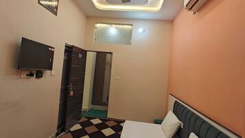 Un dormitorio con cama, ventilador de techo, aire acondicionado, televisor y una puerta que da a otra habitación.