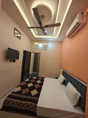 A bedroom with a bed, ceiling fan, air conditioning unit, television, and a door leading to another room.