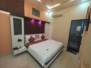 A hotel room with a bed, bedside table, air conditioning unit, and a bathroom visible through an open door. - HOTEL PINK CITY (Sikar)