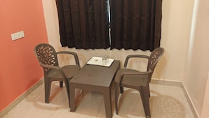 A small room with a table and two chairs, a window with black curtains, and a wall socket. - HOTEL PINK CITY (Sikar)
