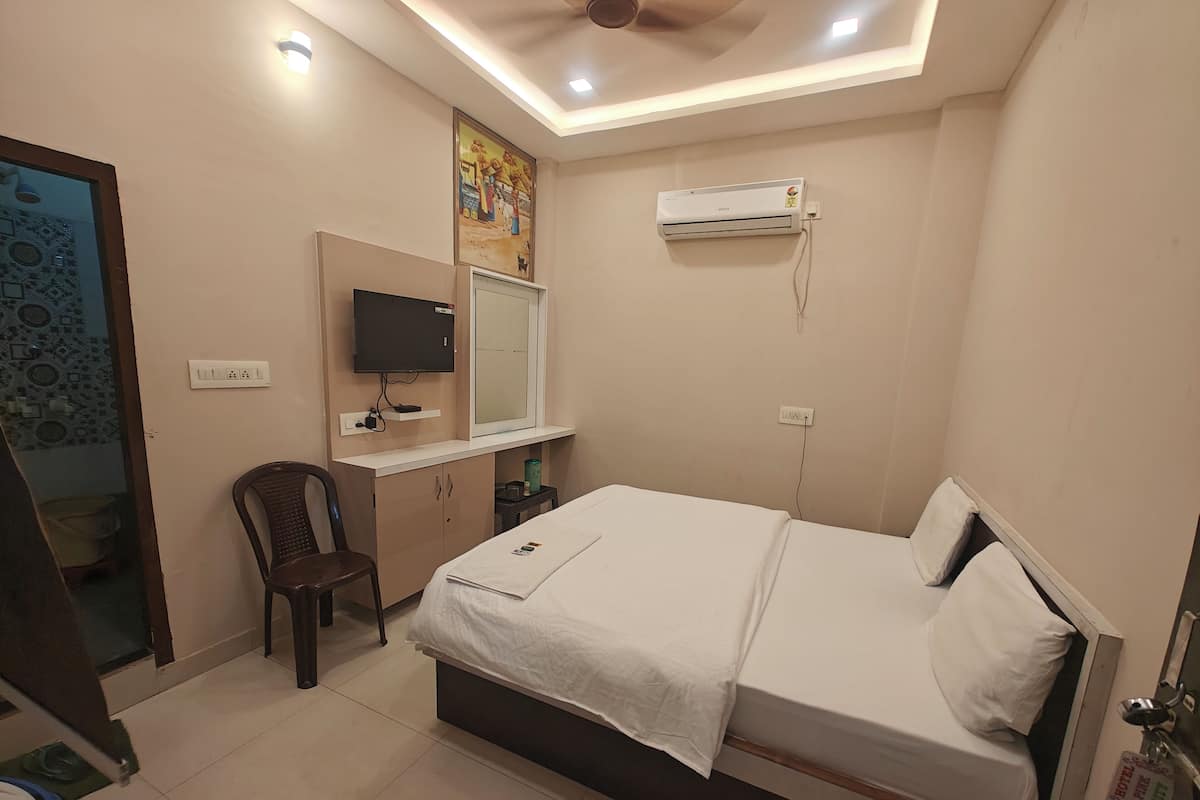 A hotel room with a bed, a desk, a chair, a TV, and an air conditioning unit.