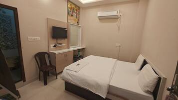 A hotel room with a bed, a desk, a chair, a TV, and an air conditioning unit.