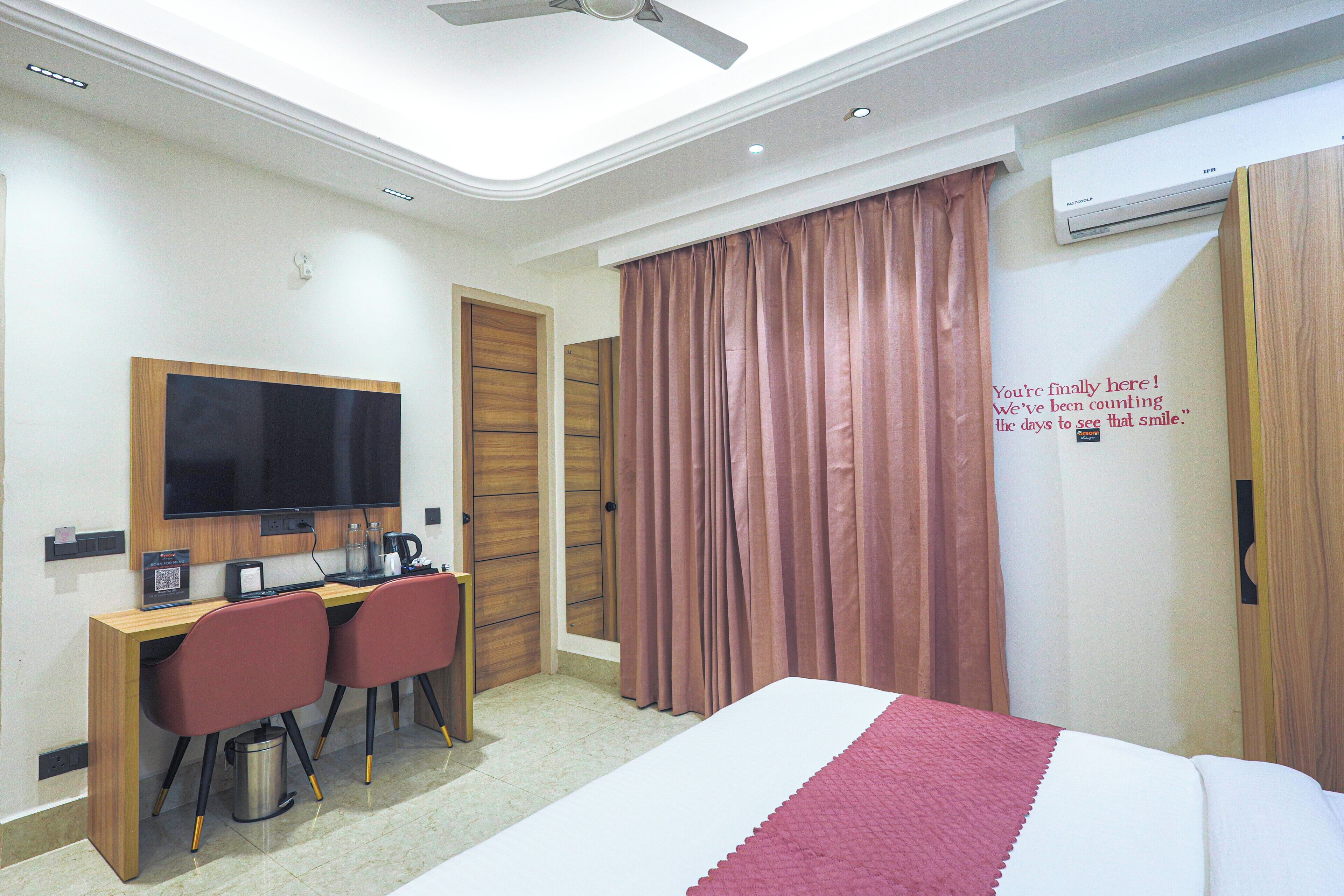 A hotel room with a bed, a desk with two chairs, a television, and an air conditioning unit.