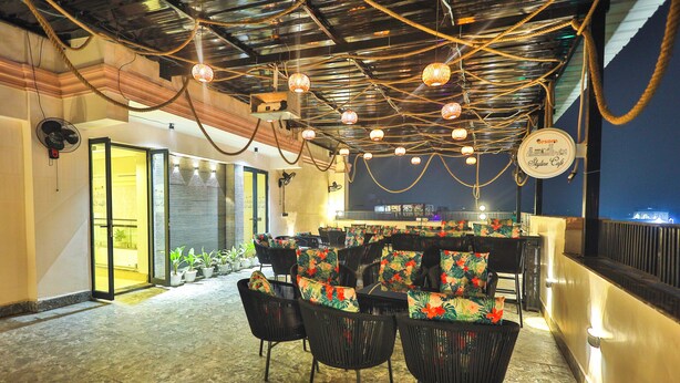 An indoor seating area with black wicker chairs, potted plants, and a bar counter. - Orsom Stays Elite Sector 53 (Gurugram)