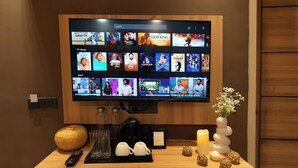 A television mounted on a wooden wall displaying various movie and TV show options. - Orsom Stays Elite Sector 53 (Gurugram)