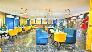 A restaurant with blue and yellow seating, marble flooring, and pendant lighting. - Orsom Stays Elite Sector 53 (Gurugram)