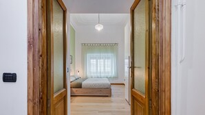 Un dormitorio con cama, piso de madera, ventana con cortinas y una lámpara colgante.