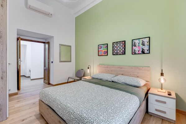 Un dormitorio con cama, mesitas de noche, una silla y una obra de arte en la pared.