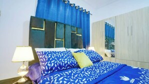 Une chambre à coucher avec un lit, une literie bleue à motifs, une table de chevet avec une lampe et une armoire.