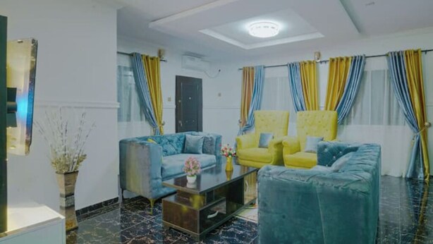 Un salon avec deux canapés, un bleu et un jaune, une table basse et une grande fenêtre avec des rideaux.