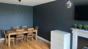 Ein Essbereich mit Holztisch und -stühlen, einem weißen Kamin und einem Wand-Fernseher.