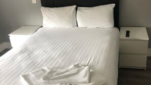 Ein ordentlich bezogenes Bett mit weißen Leinen und Kissen, ein dunkles Kopfteil und zwei Nachttische, auf einem liegt eine Fernbedienung.