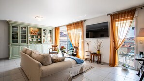 Un soggiorno con divano, televisore, mobile vetrina e balcone con tende.