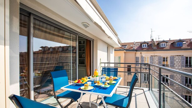 Un balcone con tavolo apparecchiato per la colazione, sedie blu e vista sulla città.