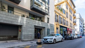 Un edificio moderno con un basculante, un'auto bianca parcheggiata davanti e una fila di auto lungo la strada.