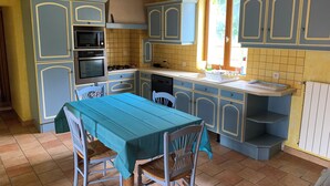 A kitchen with blue cabinets, a table with a green tablecloth, and a window with a view of greenery. - Country house close to town (Champfleur)