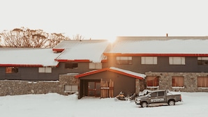 A building with a stone foundation and a red roof, a garage, and a parked truck. - 3 Share - 3 Share Room - Perisher Village Views (Perisher Valley)