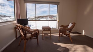 A room with a large window, two wicker chairs, a small table, and a television.