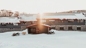 A snow-covered building with a stone facade and a red roof. There are two snowmobiles parked in front.