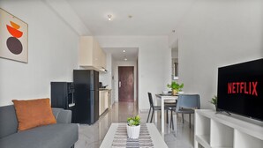 Ein modernes Wohnzimmer mit einer Couch, einem Couchtisch mit Pflanze, einem Fernseher der 'NETFLIX' zeigt und einer Küche im Hintergrund.