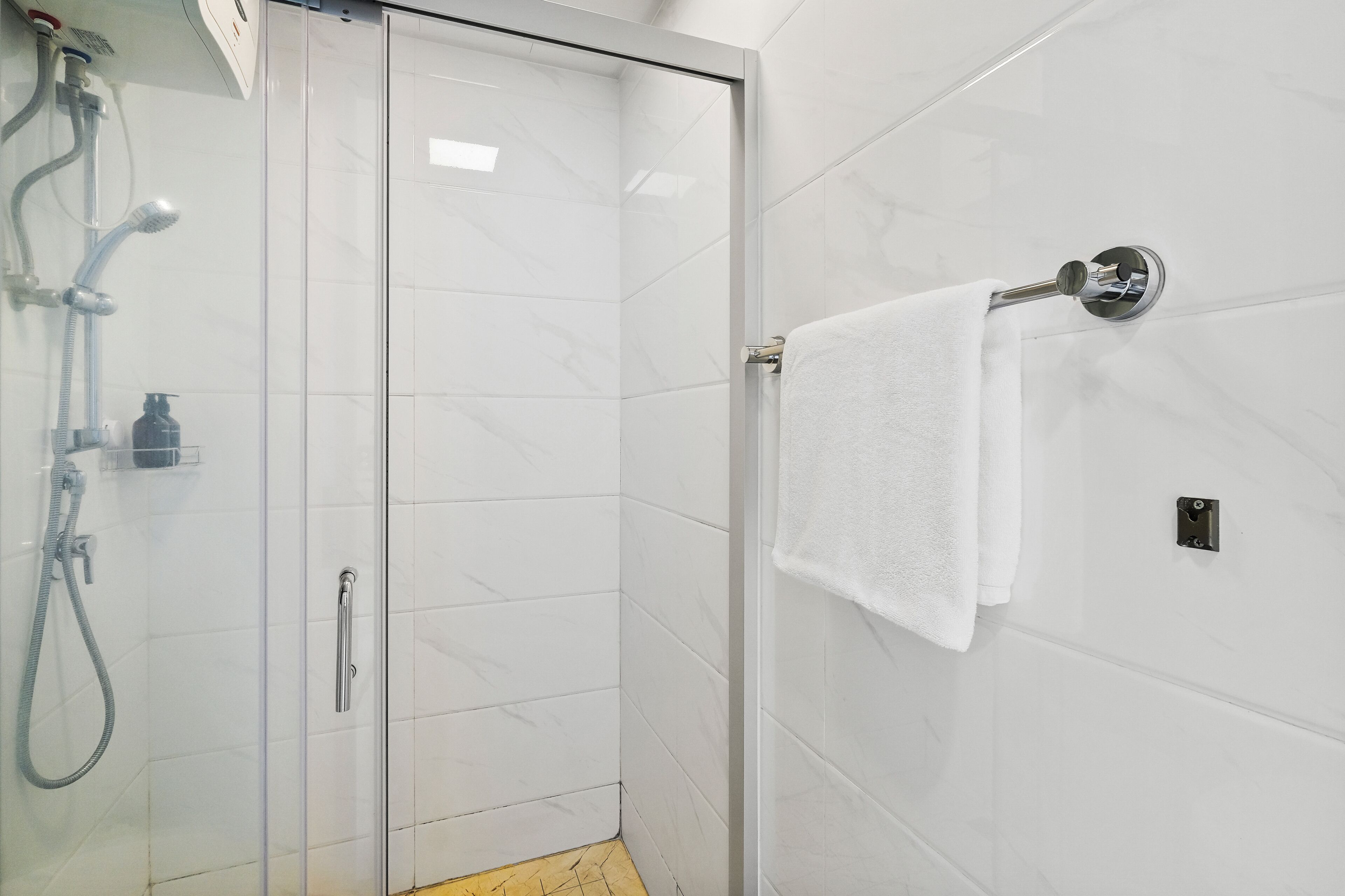 Een moderne badkamer met een douchecabine van glas, een witte handdoek aan een metalen handdoekhouder en een zichtbare douchekop.