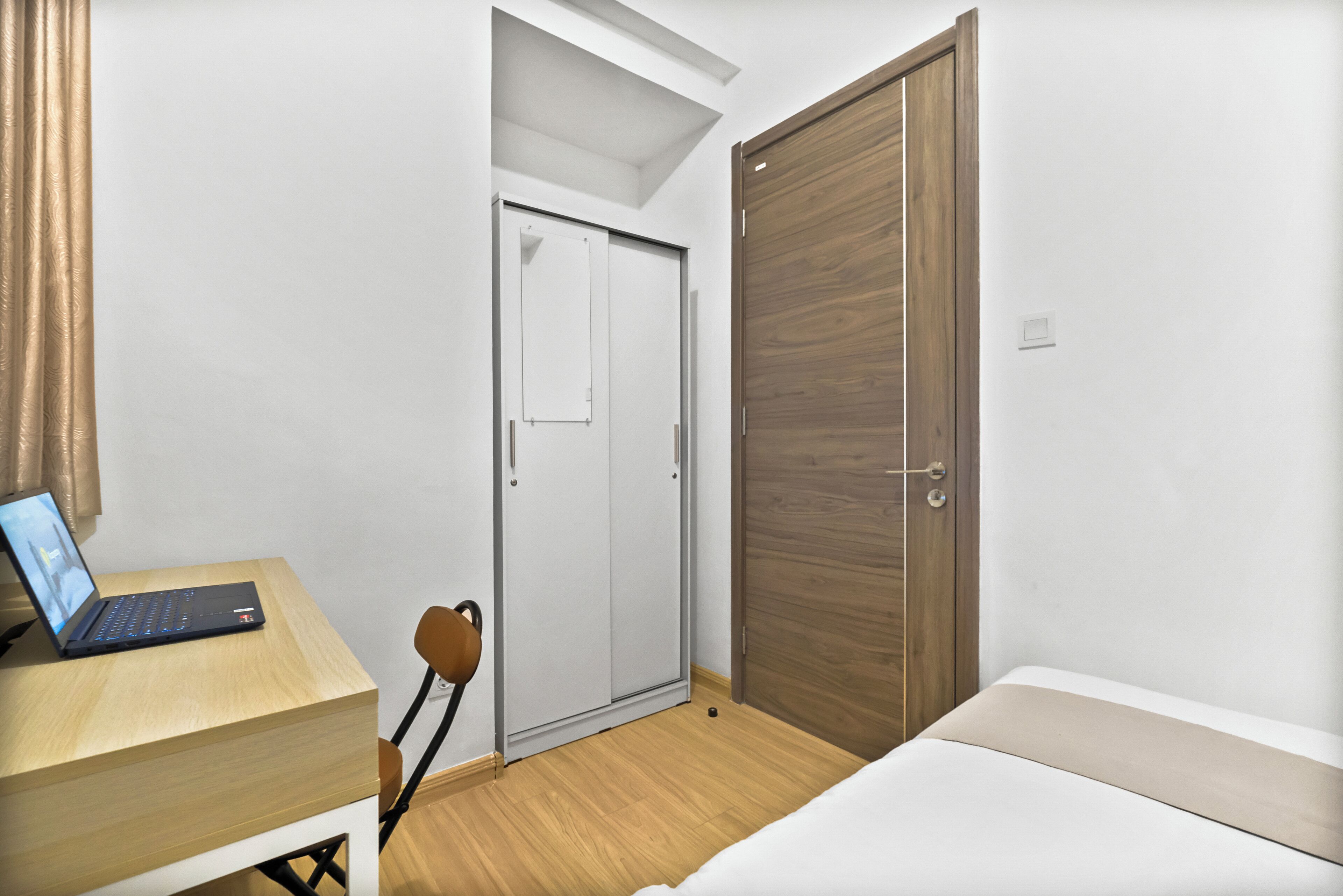 A room with a bed, a desk with a laptop, a wardrobe, and a chair.