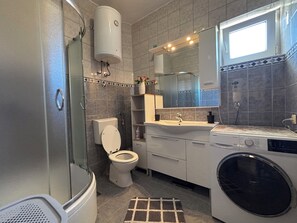 A modern bathroom with a glass-enclosed shower, a toilet, a sink, a mirror, and a washing machine. - Apartment Lu&Ni (Crikvenica)