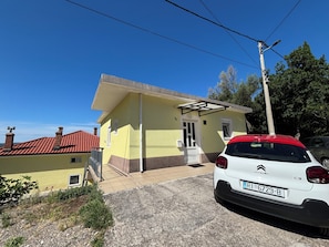 A yellow building with a red roof, a white car parked in front, and a clear blue sky. - Apartment Lu&Ni (Crikvenica)