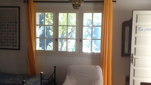 A room with a bed, a chair, a table, a window with curtains, and a ceiling light fixture.