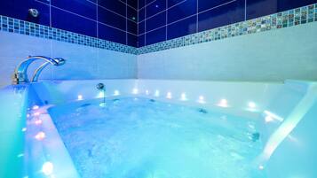 Bathroom features a large bathtub with a chrome faucet and control knob, surrounded by recessed lighting and blue-tiled mosaic walls.
