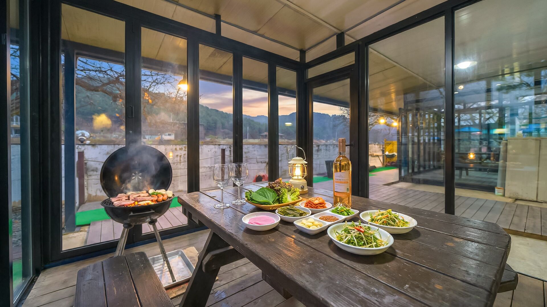 Area esterna con tavolo da pranzo, barbecue, piatti di cibo, una bottiglia di vino e una lanterna.