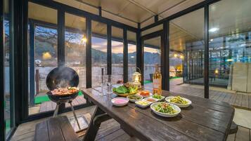 An outdoor dining area with a grill, table set with plates of food, a bottle of wine, and a lantern.