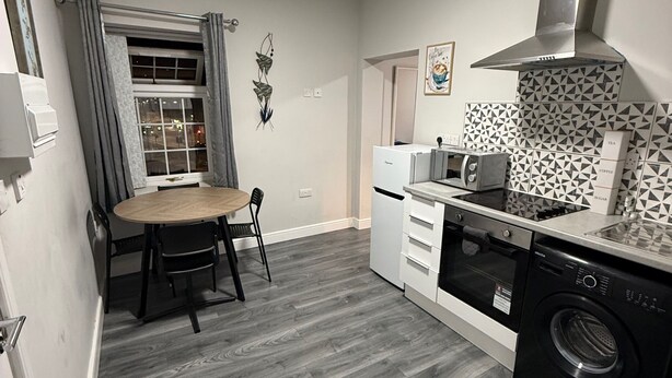 A compact kitchen with a dining table, a built-in oven, a washing machine, and a patterned backsplash.