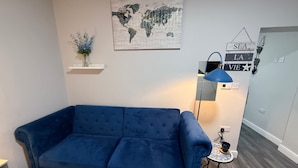 A living room with a blue sofa, a world map on the wall, a small table with a lamp, and a decorative sign.