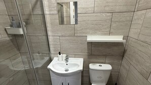 A bathroom with a shower, toilet, sink, and a small mirror.