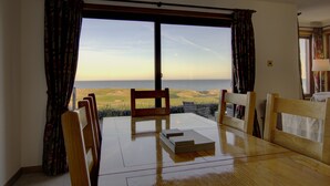 A dining area with a table and chairs, a view of the ocean, and a window with curtains. - 2 Links View Brora in Brora (Brora)