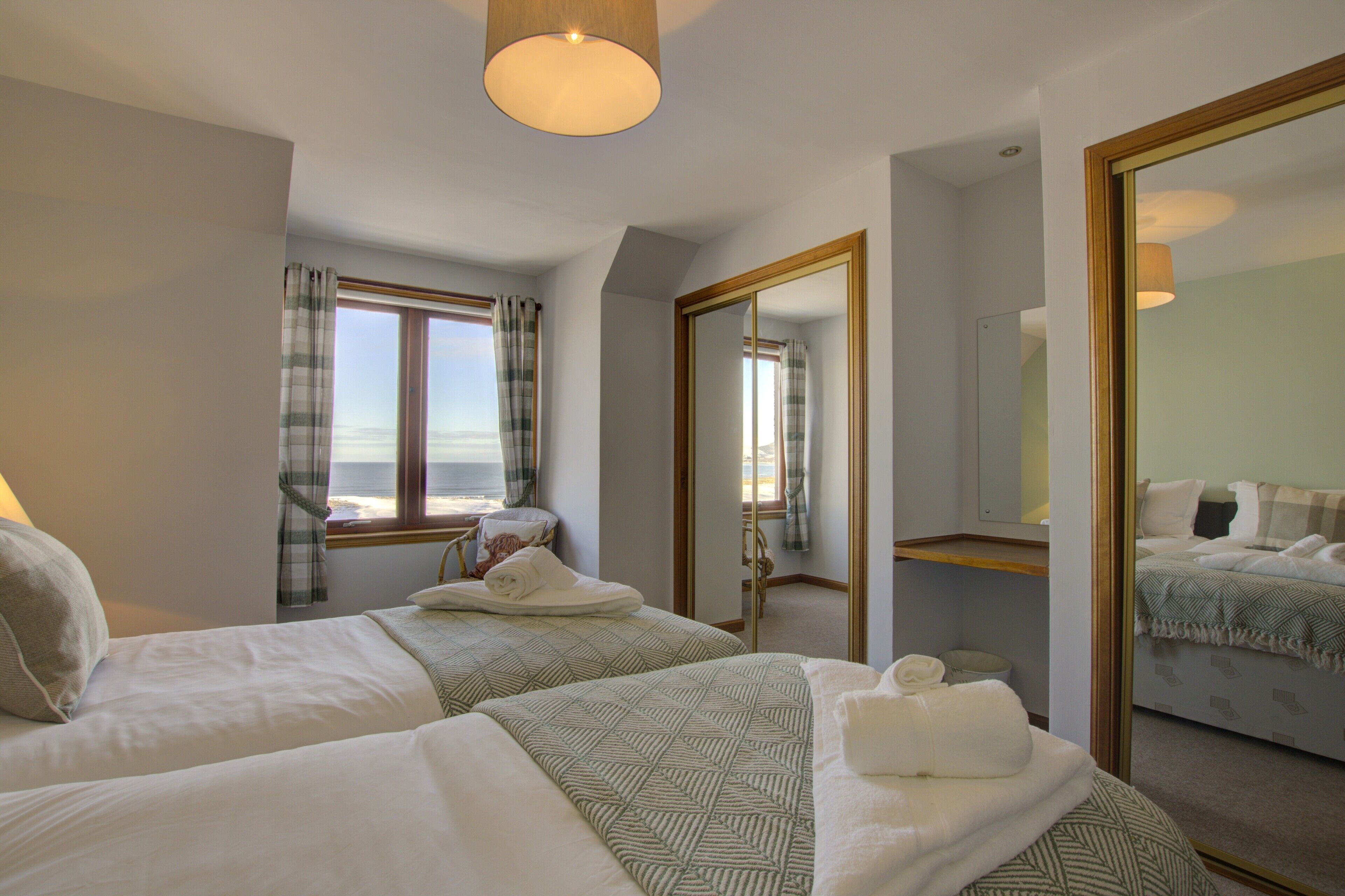 A hotel room with two beds, a large mirror, and a view of the sea through a window.