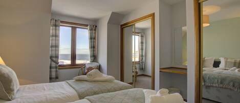 A hotel room with two beds, a large mirror, and a view of the sea through a window.