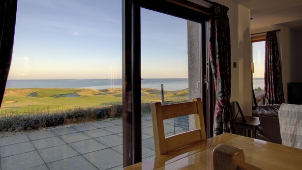 A room with a large sliding glass door leading to a balcony with a view of a golf course and the ocean. - 2 Links View Brora in Brora (Brora)