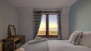 A bedroom with a large bed, a wooden nightstand, a framed mirror, and a window with curtains. - 2 Links View Brora in Brora (Brora)