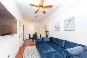 A modern living room with a blue sectional sofa, a ceiling fan, and artwork on the walls.